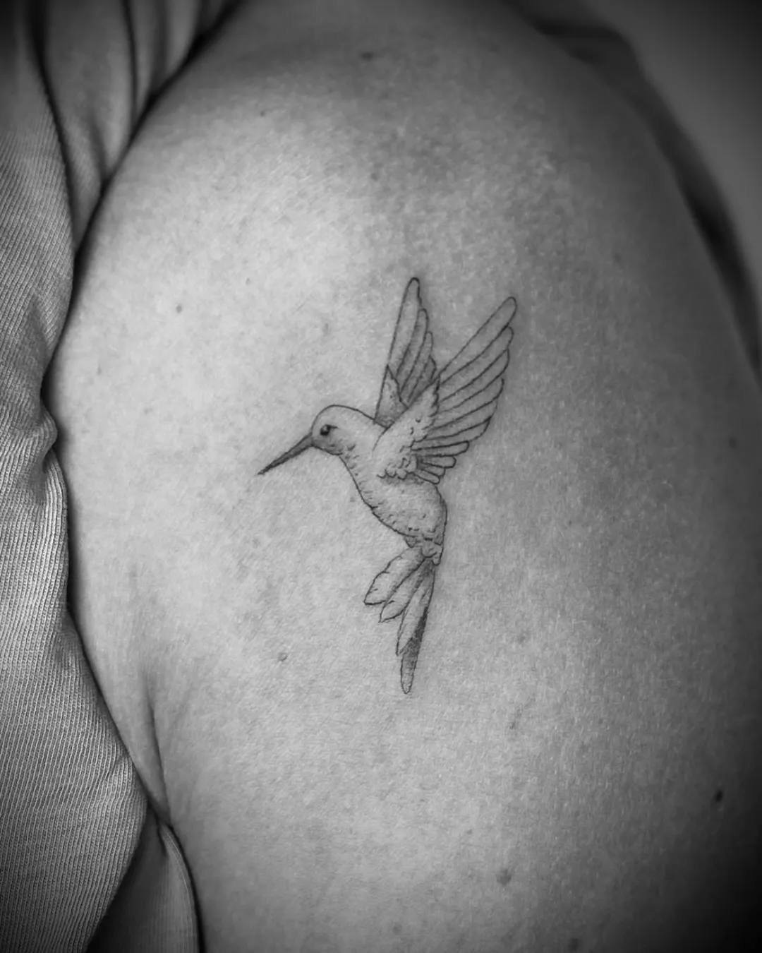 Fineline-Tattoo: schwebender Kolibri auf dem Oberarm